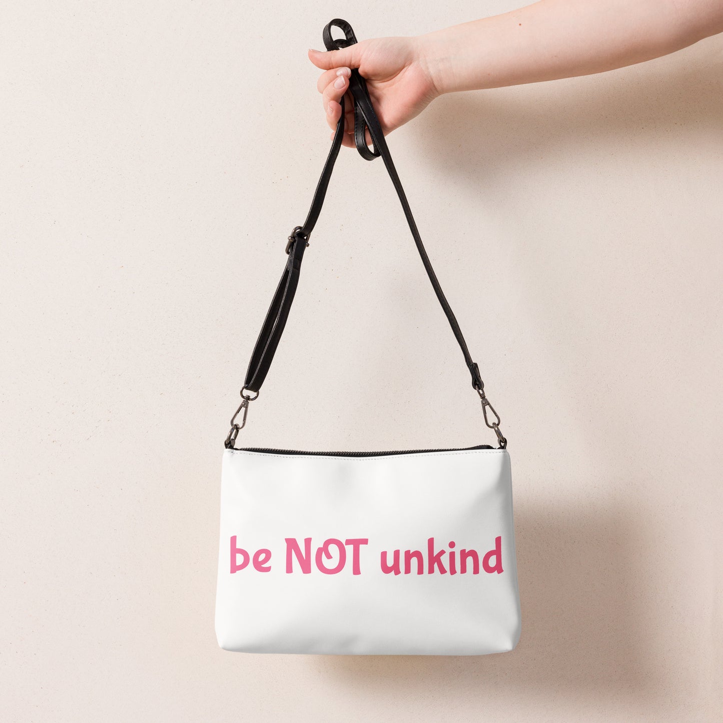 White bag with 'be NOT unkind' text held by a hand against a beige background