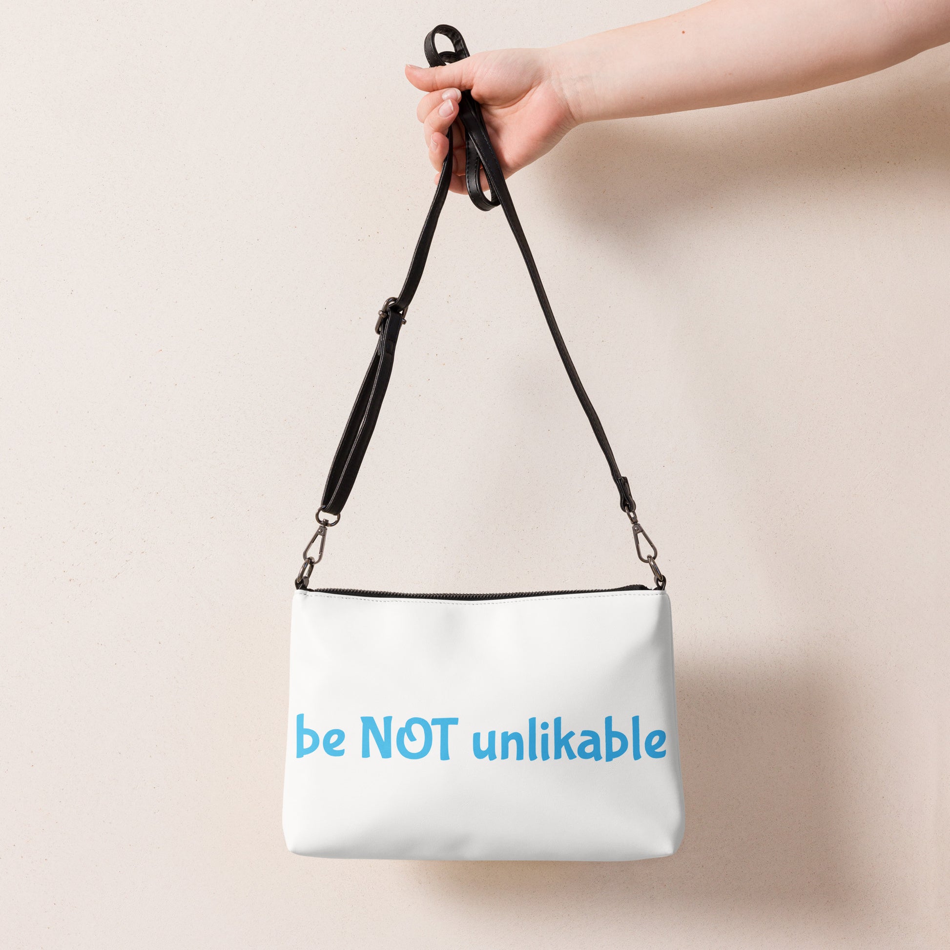 White bag with 'be NOT unlikable' text held by a hand against a beige background