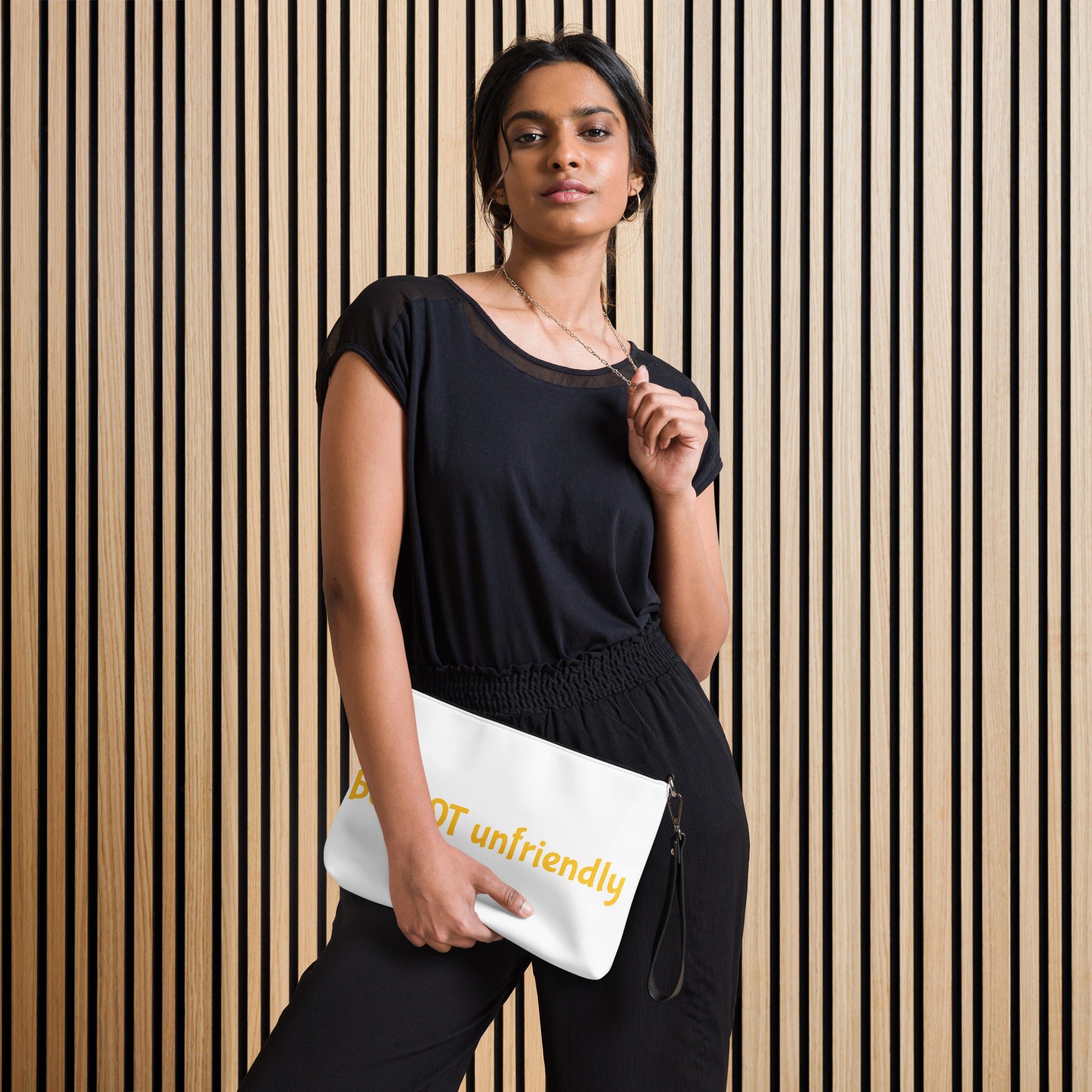 Woman holding a white clutch with 'be not unfriendly' text design against a striped wall.