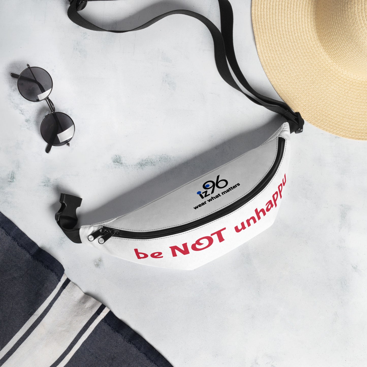 White bag with 'be NOT unhappy' text, sunglasses, and a hat on a marble surface