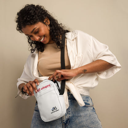 Woman holding a white bag with text 'be not unhappy' and logo against a beige background