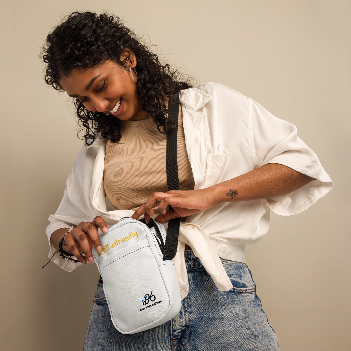 Woman holding a white crossbody bag with a visible brand logo against a beige background