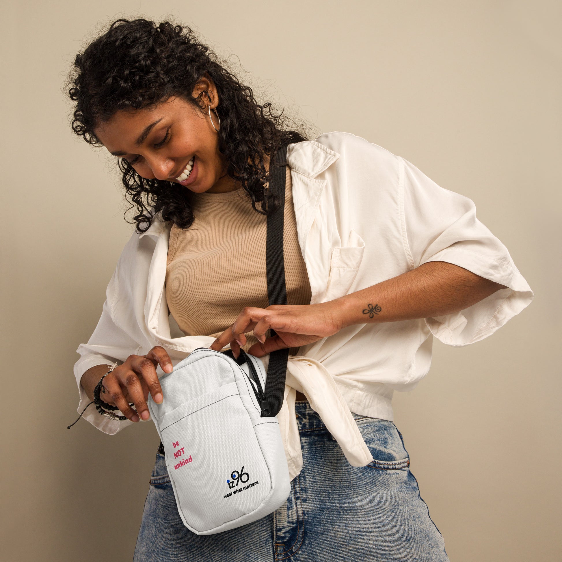 Woman holding a white crossbody bag with a visible brand logo against a beige background