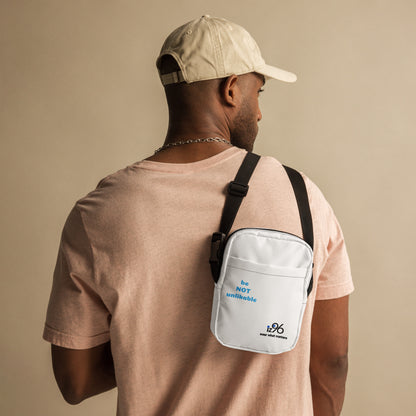 Man wearing a beige cap and light pink shirt with a white crossbody bag on a beige background