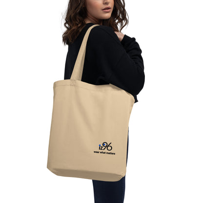 Beige tote bag with a logo worn by a person on a white background