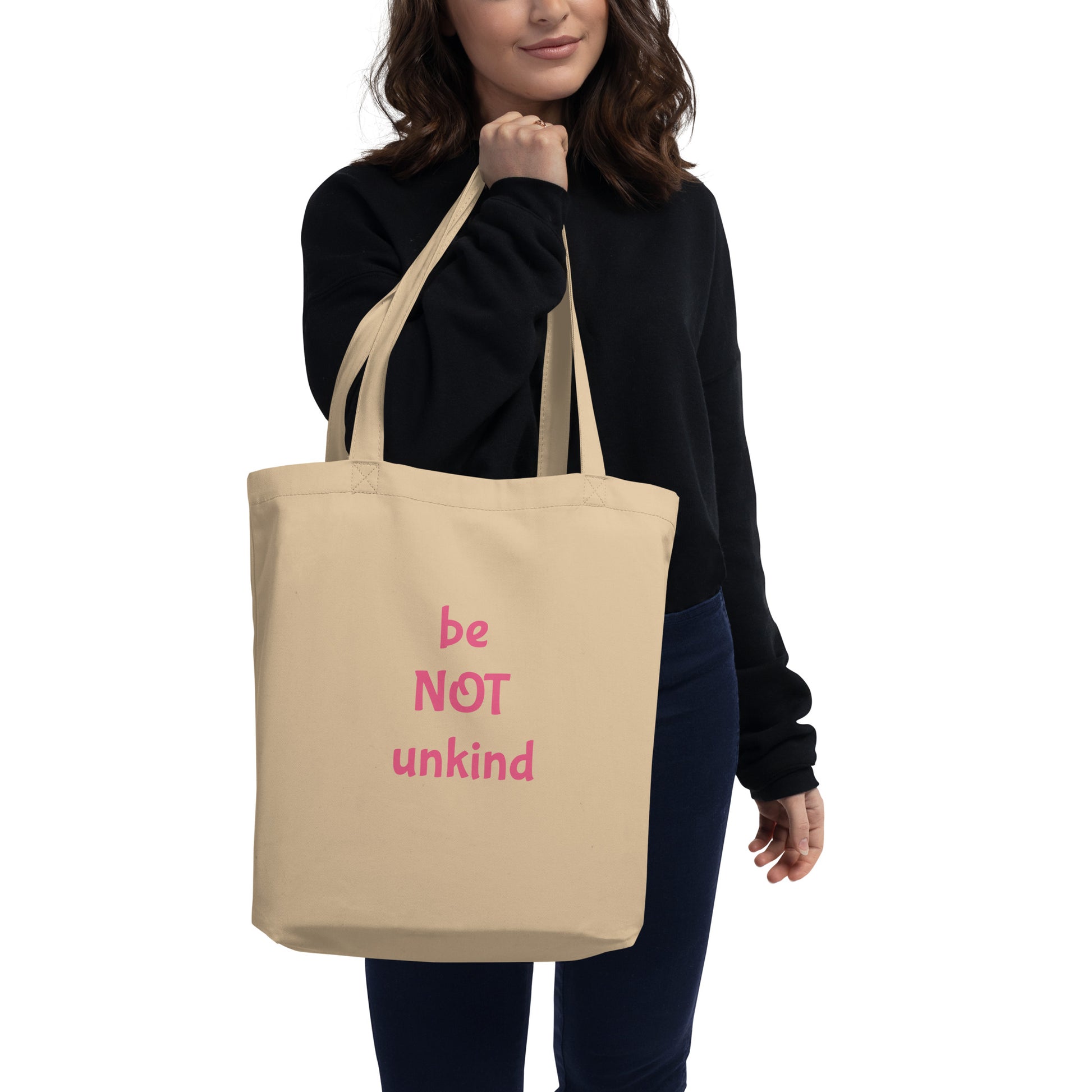 Person holding a beige tote bag with 'be not unkind' branding on a white background