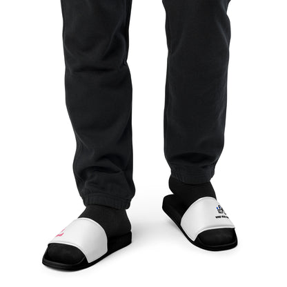Black and white slippers with text and logo design worn by a person in black pants on a white background