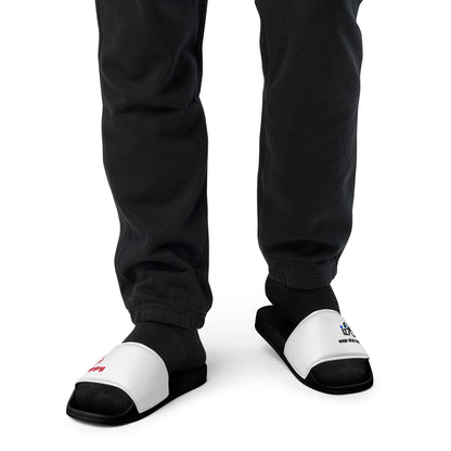 Black and white slippers with a text and logo design worn by a person in black pants on a white background