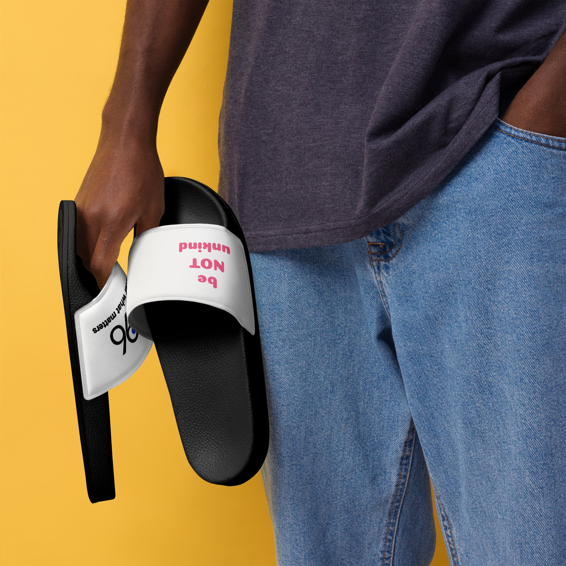 Person holding a black slide sandal with white sole against a yellow background