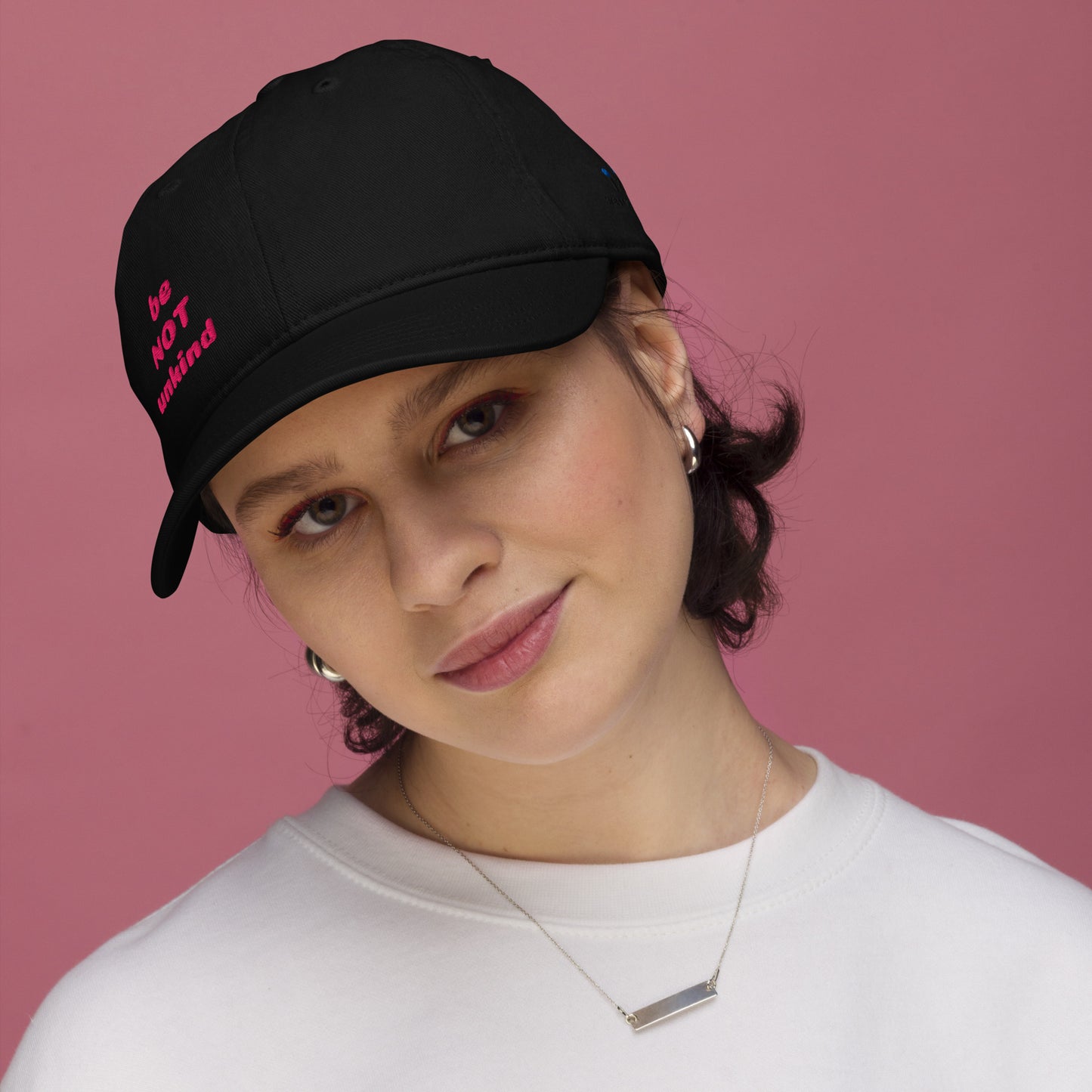 Person wearing a black cap with pink text against a pink background