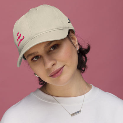 Woman wearing a beige cap with 'be not unkind' text against a pink background