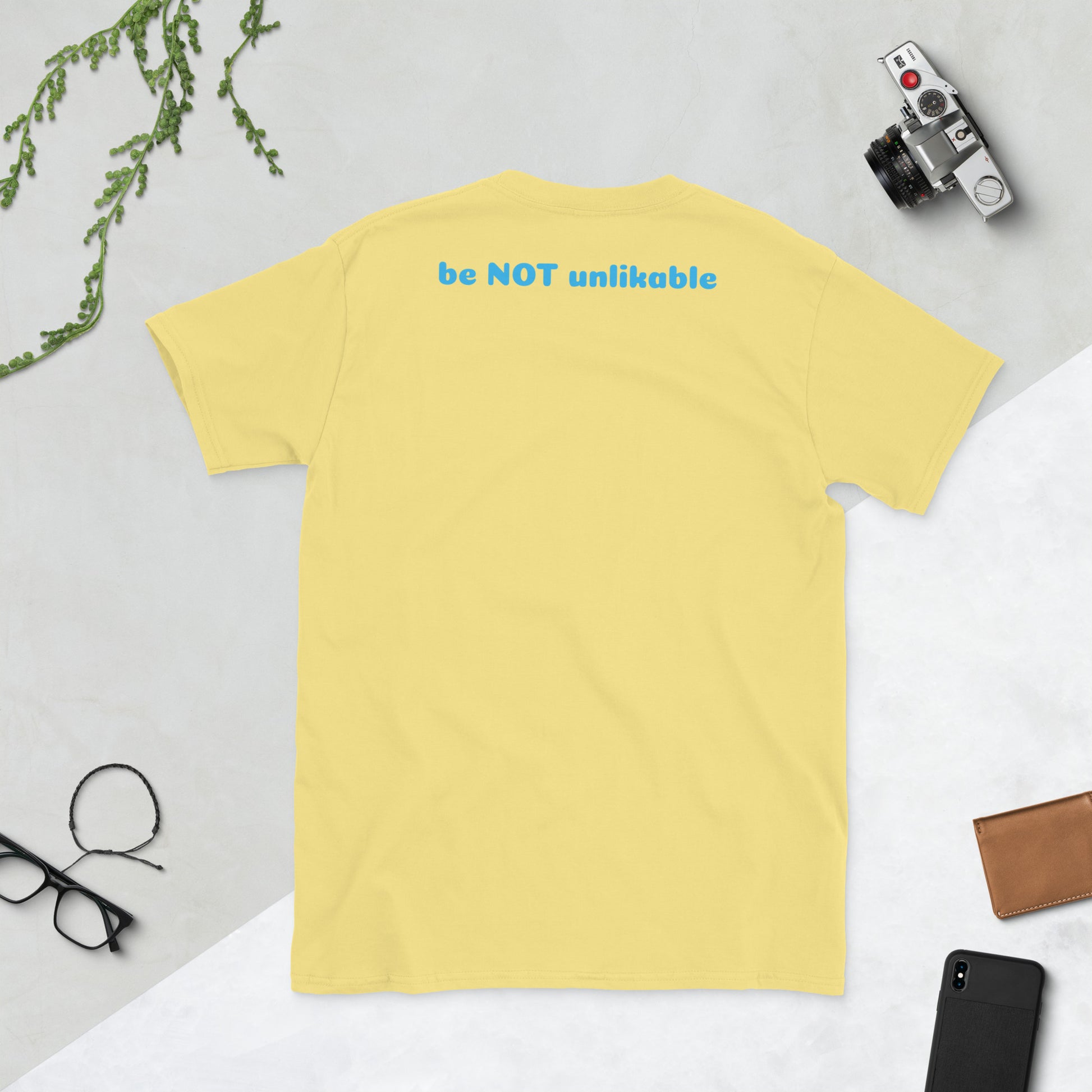 Yellow t-shirt on a light gray surface with a phone, wallet, and glasses.