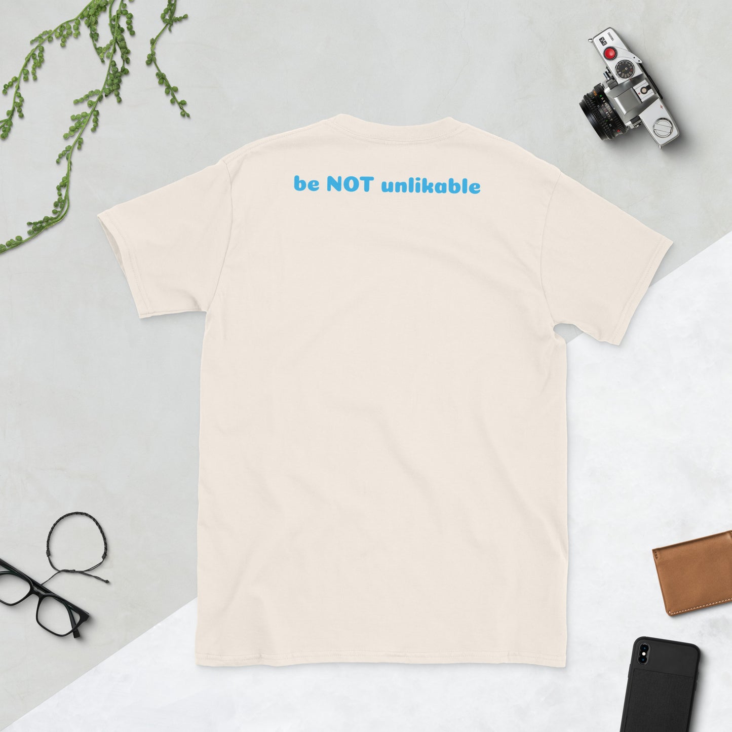 Beige t-shirt on a light gray surface with a camera, phone, and glasses.
