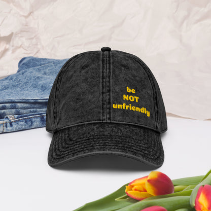 Black cap with 'be NOT unfriendly' text, denim jacket, and tulips on a light background