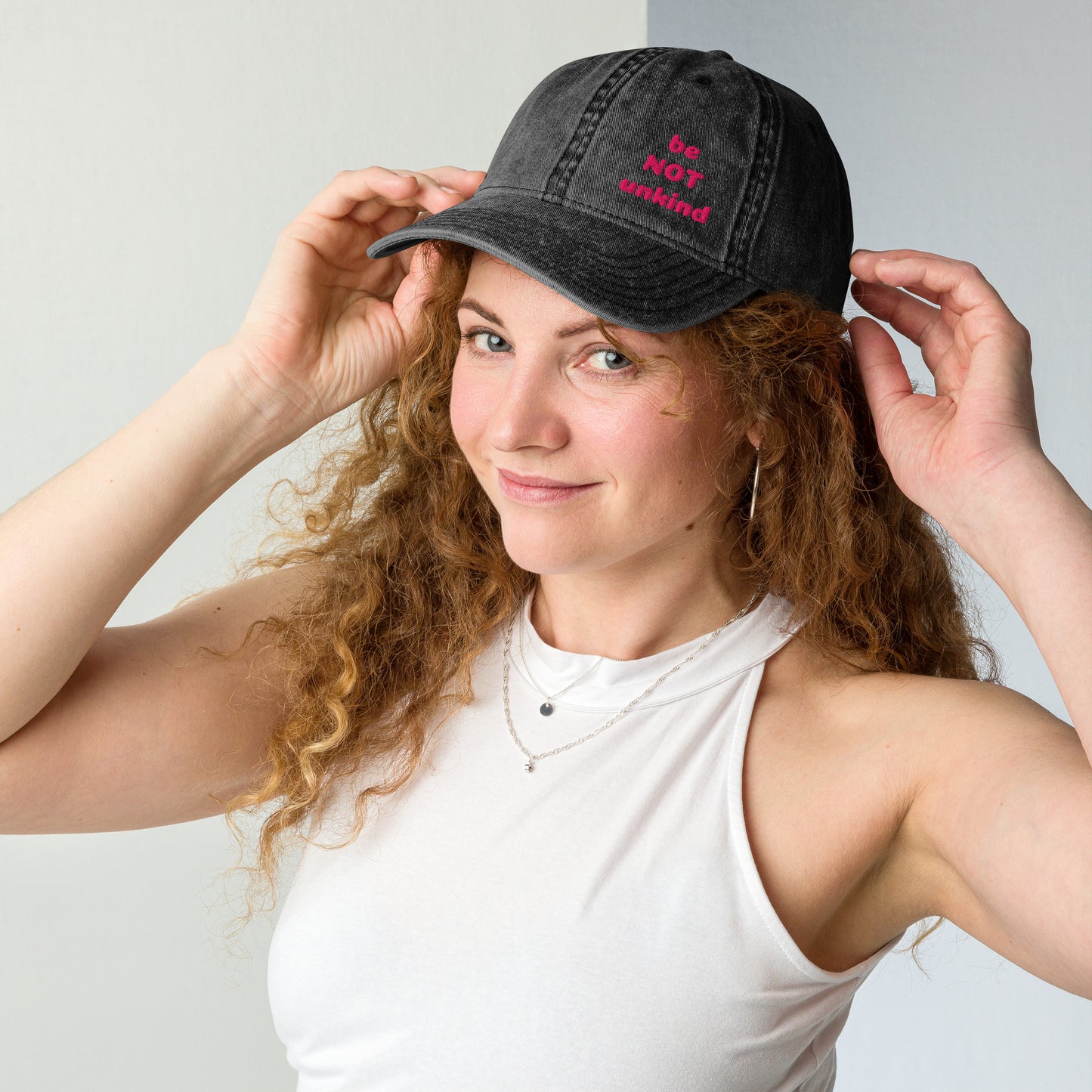 Woman wearing a black denim cap with a white logo against a light gray background