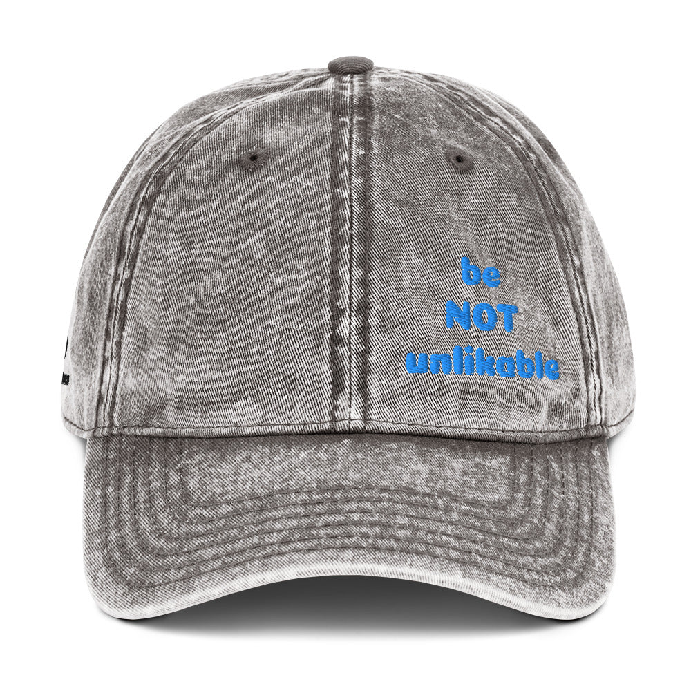 Gray denim cap with 'be NOT unlikeable' text in blue on a white background