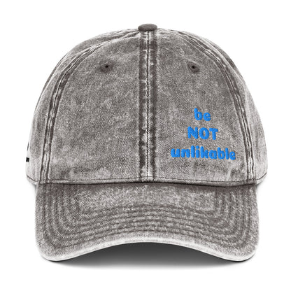 Gray denim cap with 'be NOT unlikeable' text in blue on a white background